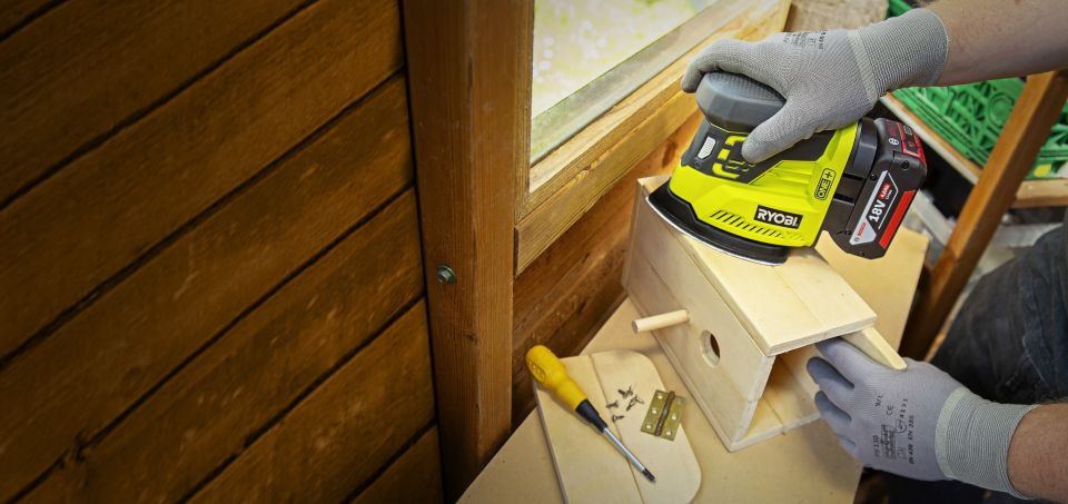 Man finishing woodworking project sanding edges of birdhouse in workshop