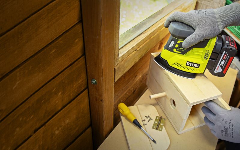 Man finishing woodworking project sanding edges of birdhouse in workshop